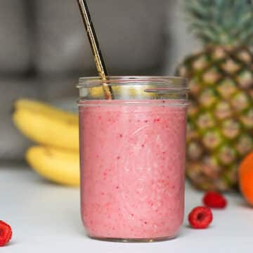 Strawberry smoothie in a mason jar glass on a white counter in front of various fruits