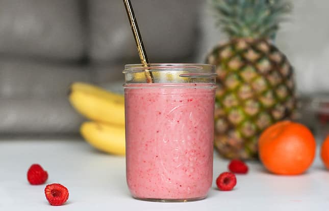 Strawberry smoothie in a mason jar glass on a white counter in front of various fruits