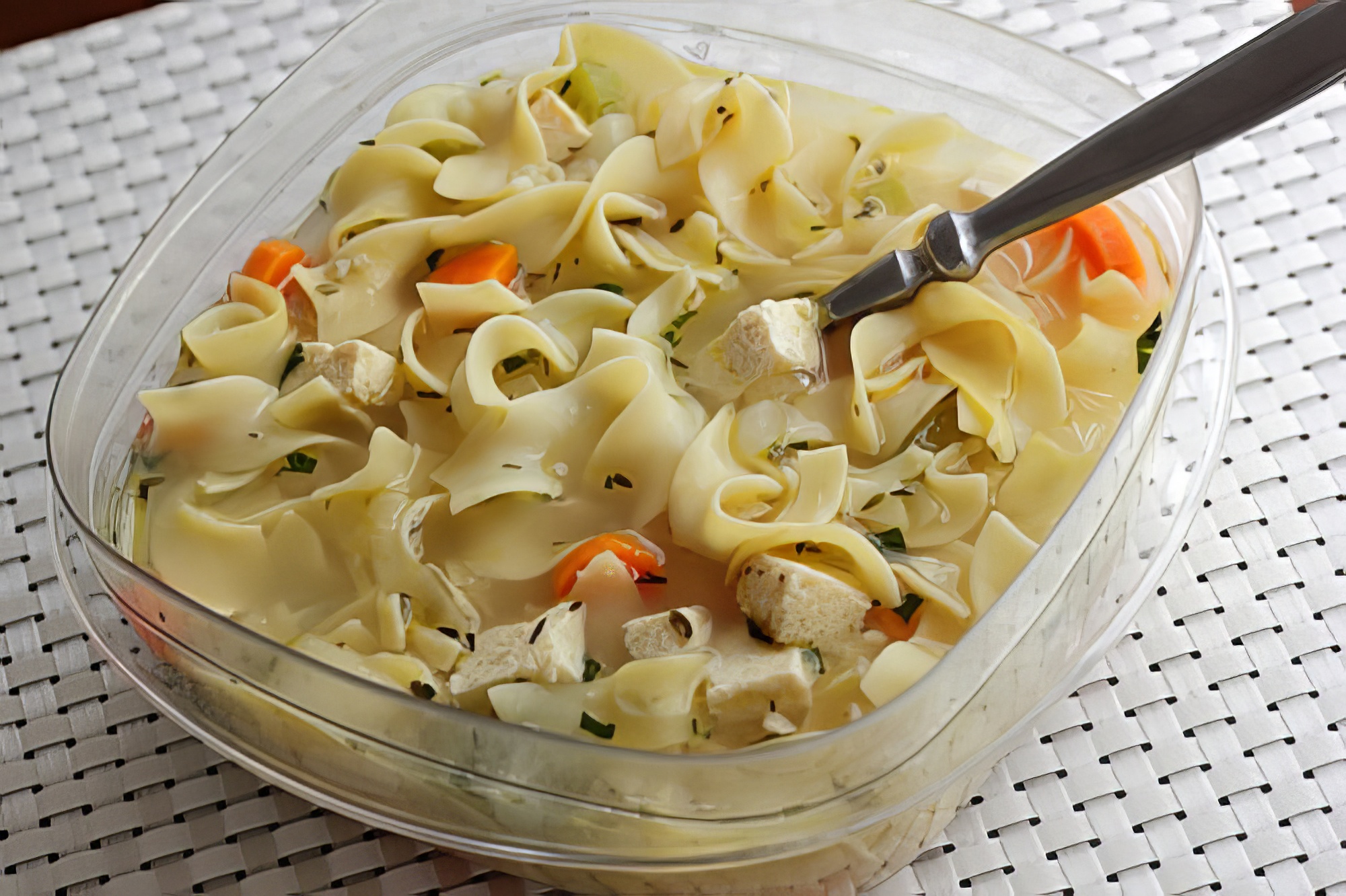 Leftover vegetarian chicken noodle soup in a glass storage container, with the noodles soaking up the broth