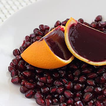 Orange wedges filled with pomegranate flavored gelatin on pomegranate seeds and a white plate