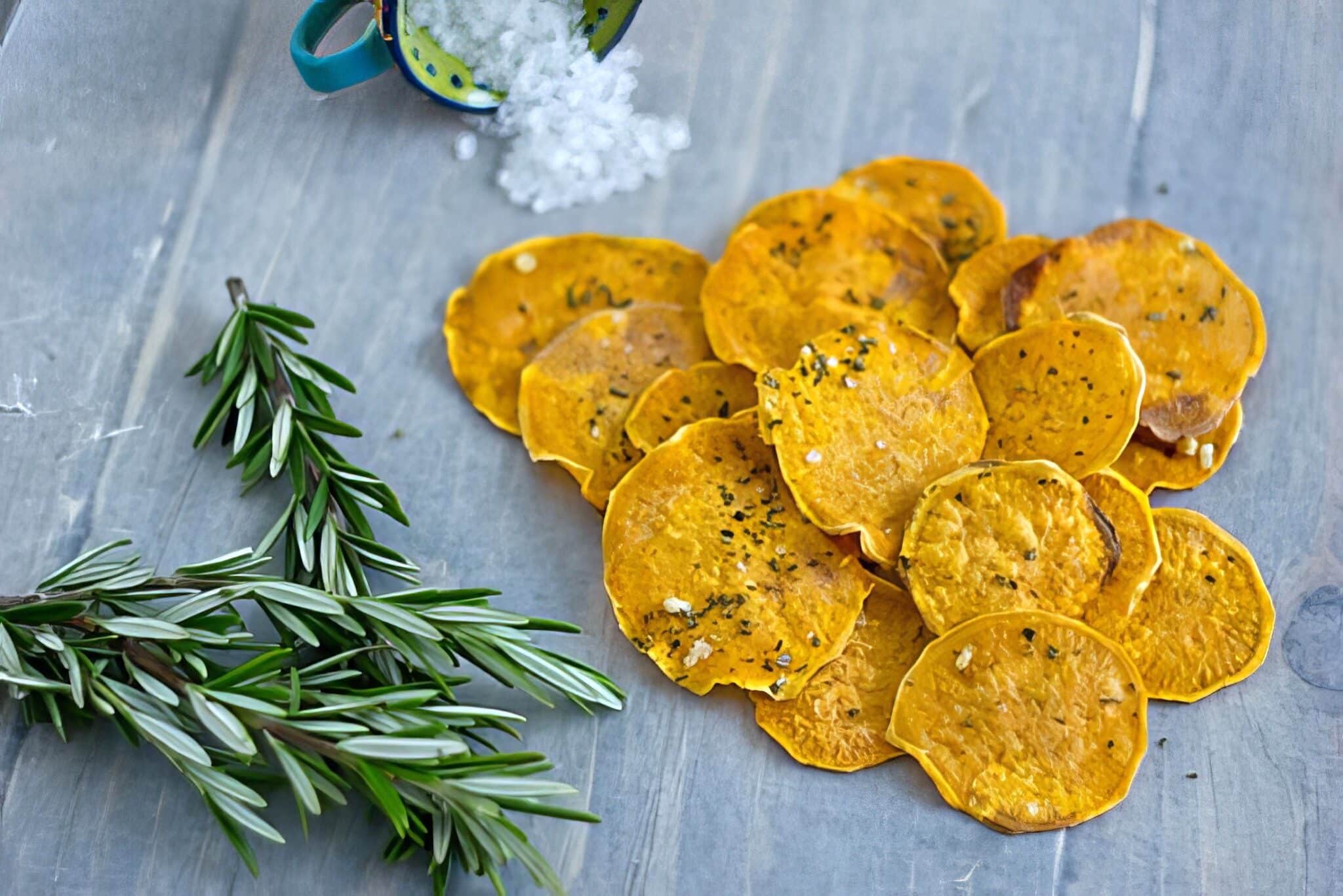 garlic rosemary sweet potato chips on a table with fresh rosemary and sea salt