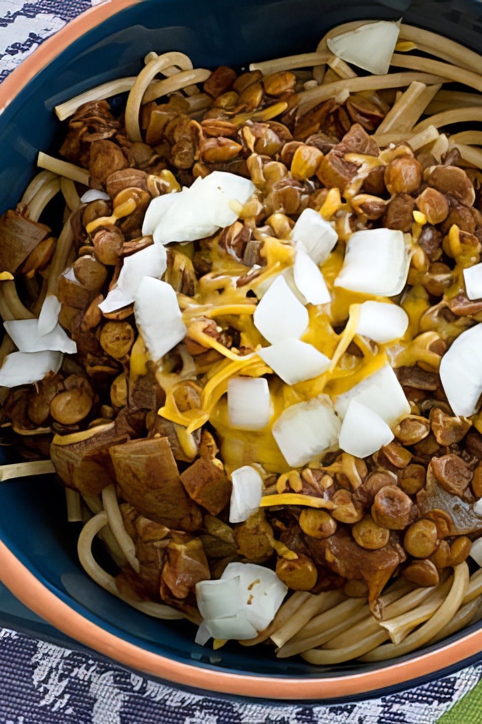 Overhead close-up of vegan Cincinnati chili with lentils, chopped onions and melted cheese over spaghetti