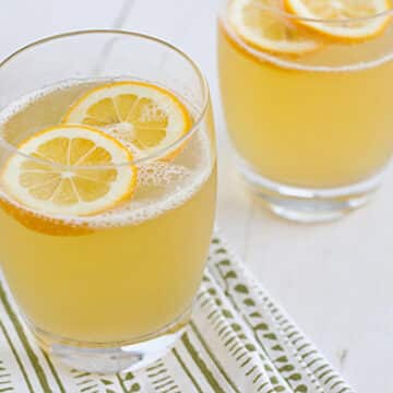 Sparkling Meyer Lemonade in glasses on a white tabletop with lemon wedges floating in them