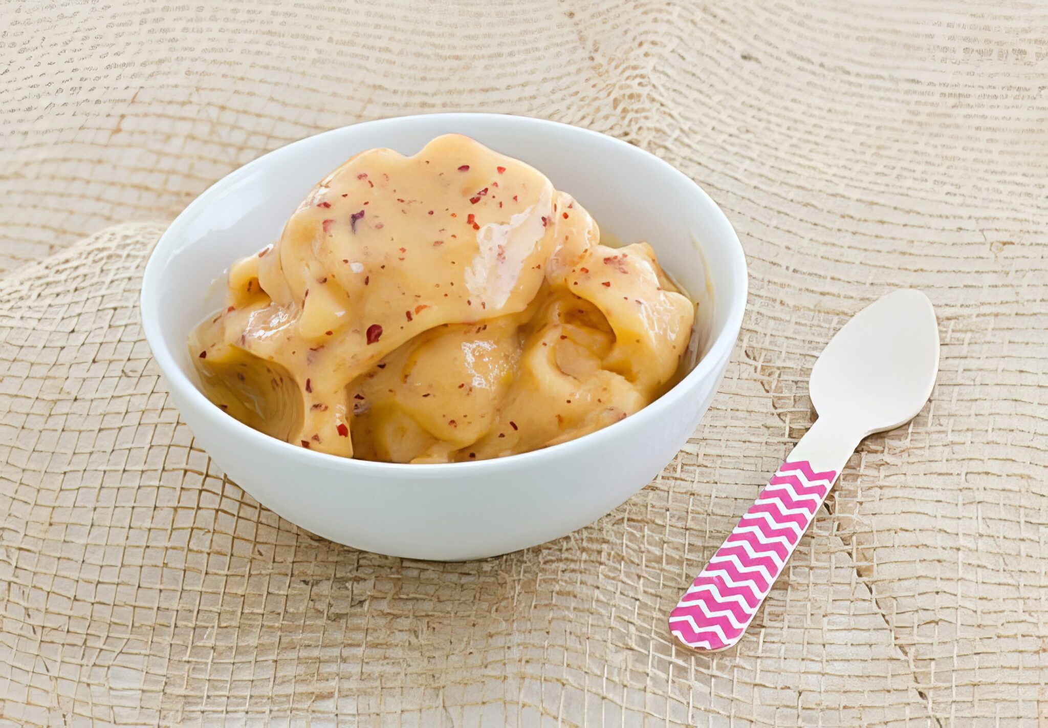 peach nice cream being served in a white bowl