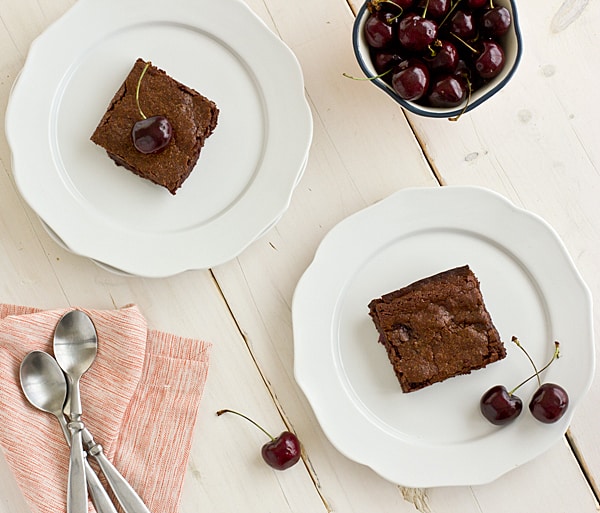 Brownies and fresh cherries rest on white china plates on a whitewashed tabletop