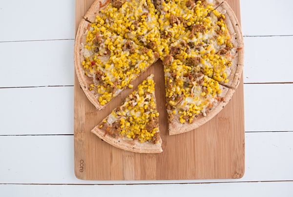 Sweet Corn, Sausage & Thyme Pizza sitting on wooden plate