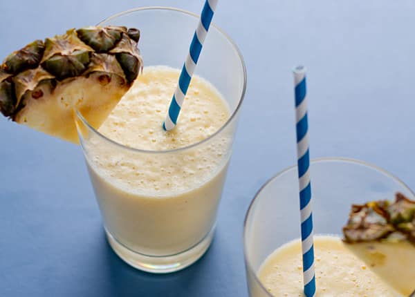Frothy pineapple smoothies in glasses on a blue surface with blue and white straws