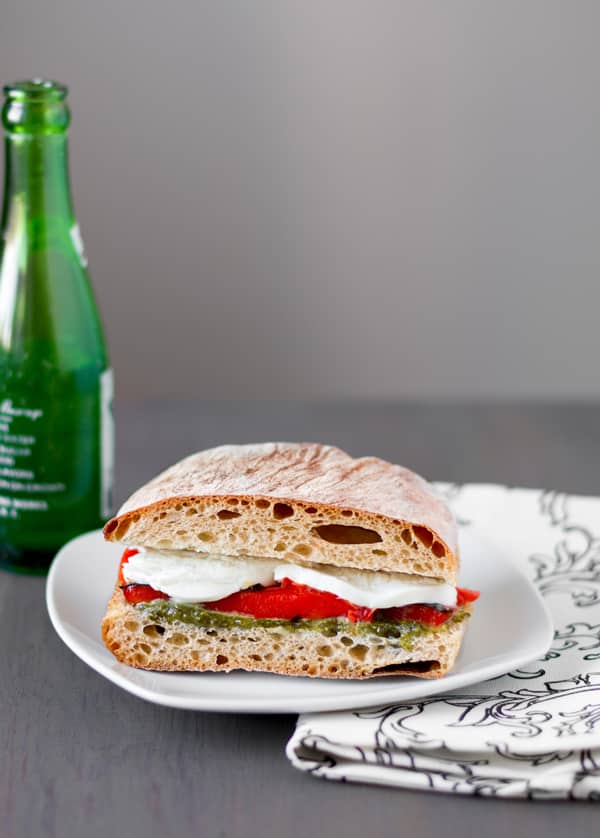 Roasted Red Pepper and Mozzarella Sandwiches with Arugula Pesto on a white plate with a green bottle and dishcloth