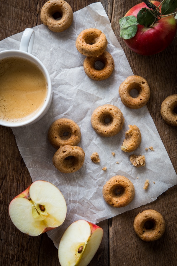 Overhead view of vegan chai-spiced apple cider doughnuts on parchment paper with coffee and sliced apples
