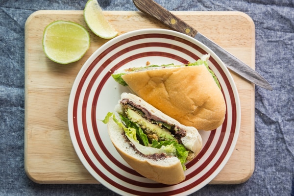 A sandwich stuffed with green veggies and black bean spread on a plate with red stripes sitting on a cutting board