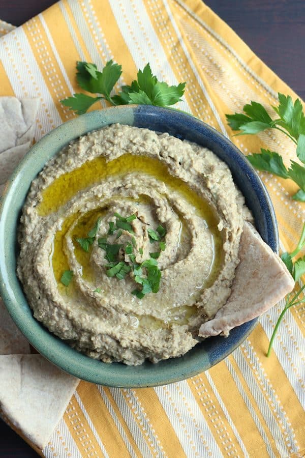 Green lentil hummus in a blue-green bowl drizzled with olive oil and chopped parsley, served with pita wedges