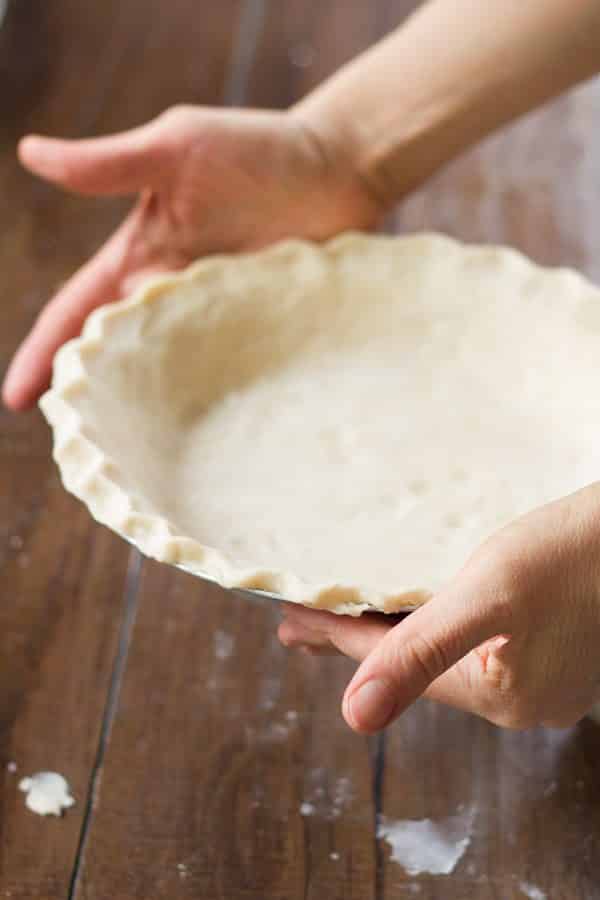 Hands holding a homemade coconut oil pie crust pressed into a pie plate