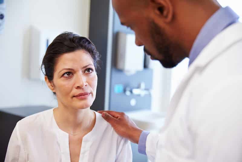 Female Patient Being Reassured By Doctor In Hospital Room