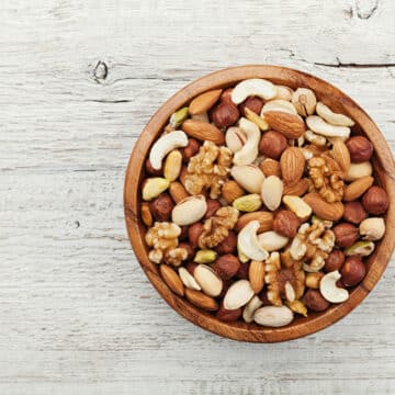 Wooden bowl with mixed nuts on white table from above. Healthy food and snack. Walnut, pistachios, almonds, hazelnuts and cashews.