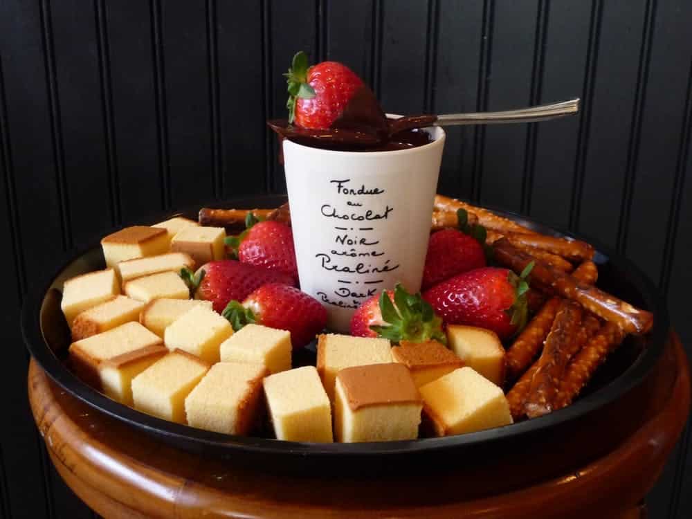 vegan fondue in a cup surrounded by strawberries, bread cubes, and pretzels for dipping