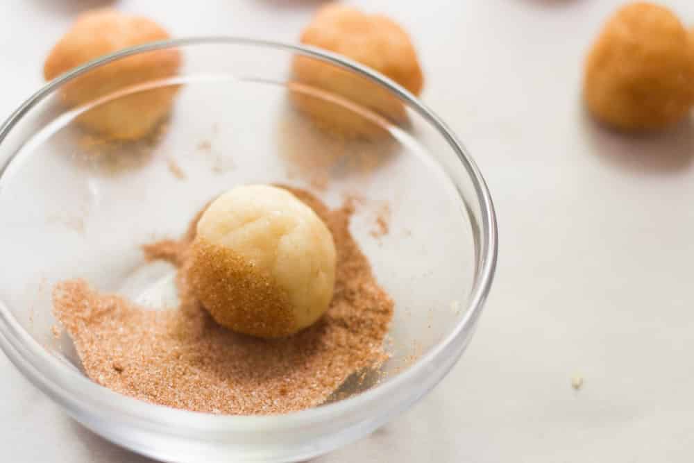 Vegan Snickerdoodle dough being rolled in cinnamon sugar