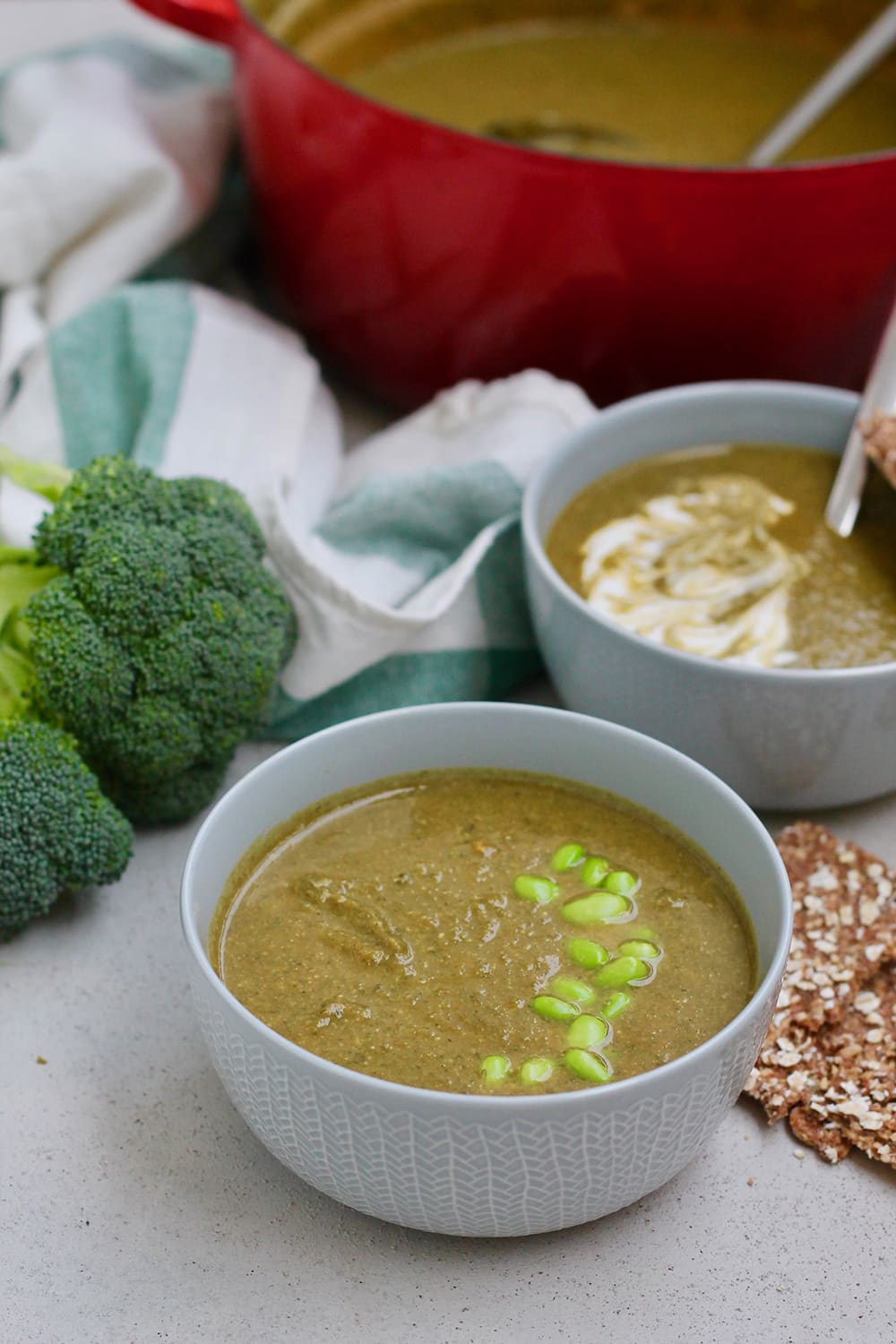 White bowls filled with hearty spinach and broccoli soup sit in front of a red soup pot also filled with soup.