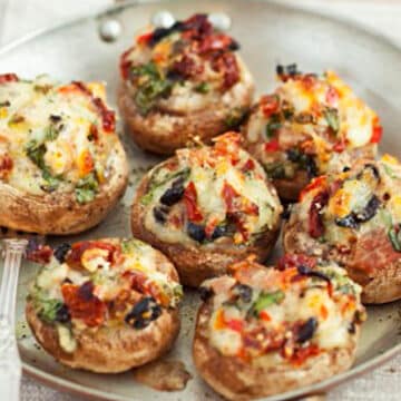 Mushroom caps stuffed with tomatoes, olives, and cheese rest on an earthenware plate on a table