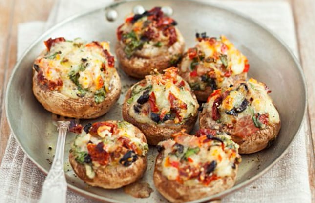Mushroom caps stuffed with tomatoes, olives, and cheese rest on an earthenware plate on a table
