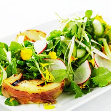 Fresh green arugula piled with grilled pears and thinly sliced raddish on a white rectangular dish