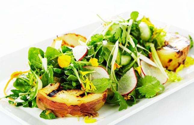 Fresh green arugula piled with grilled pears and thinly sliced raddish on a white rectangular dish