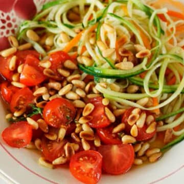 Carrot and Zucchini strips garnished with marinated tomatoes and pine nuts on a white plate