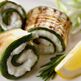 Grilled zucchini strips wrapped around a ricotta-herb filling next to a lemon slice