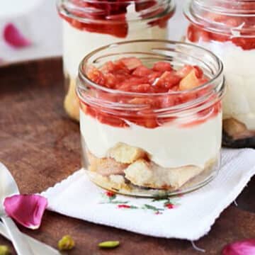 Rhubarb-topped parfaits in mason jars on a wooden surface sprinkled with rose petals