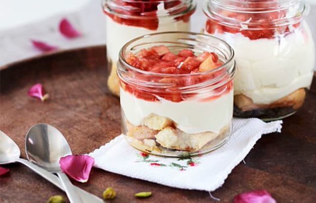Rhubarb-topped parfaits in mason jars on a wooden surface sprinkled with rose petals