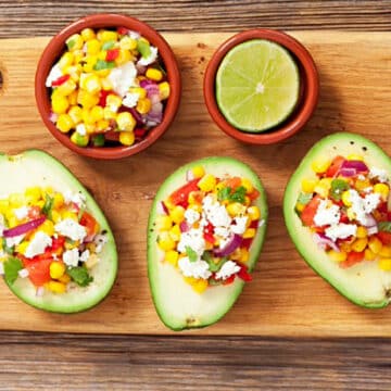 Avocado halves on a wooden cutting board filled with corn salsa and queso blanco cheese