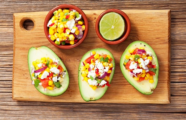 Avocado halves on a wooden cutting board filled with corn salsa and queso blanco cheese