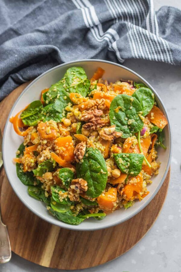 Overhead view of a pumpkin chickpea quinoa bowl with baby spinach and walnuts on a wooden board