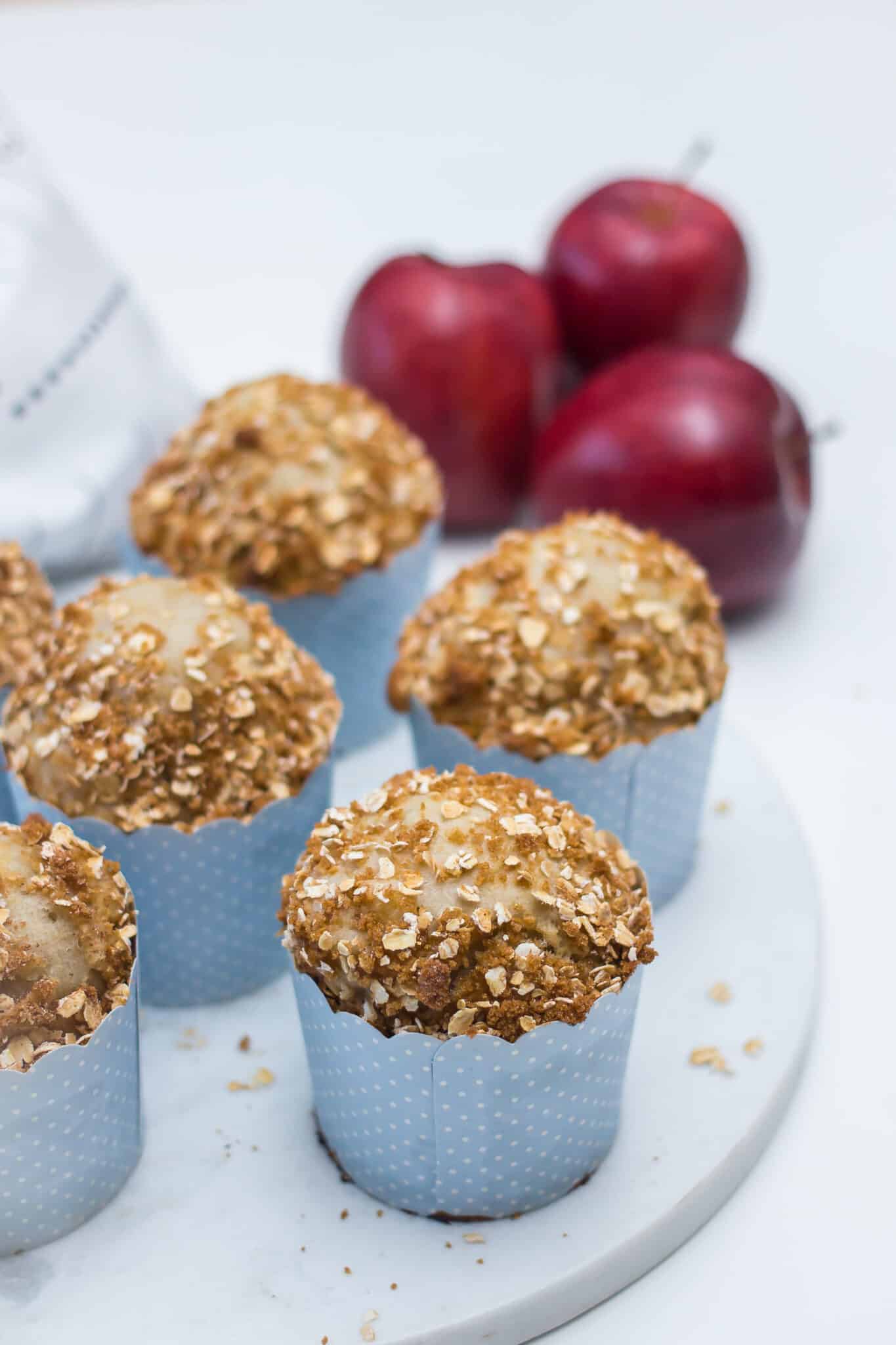Apple and cottage cheese muffins with oat streusel tops in blue paper liners, with red apples in the background