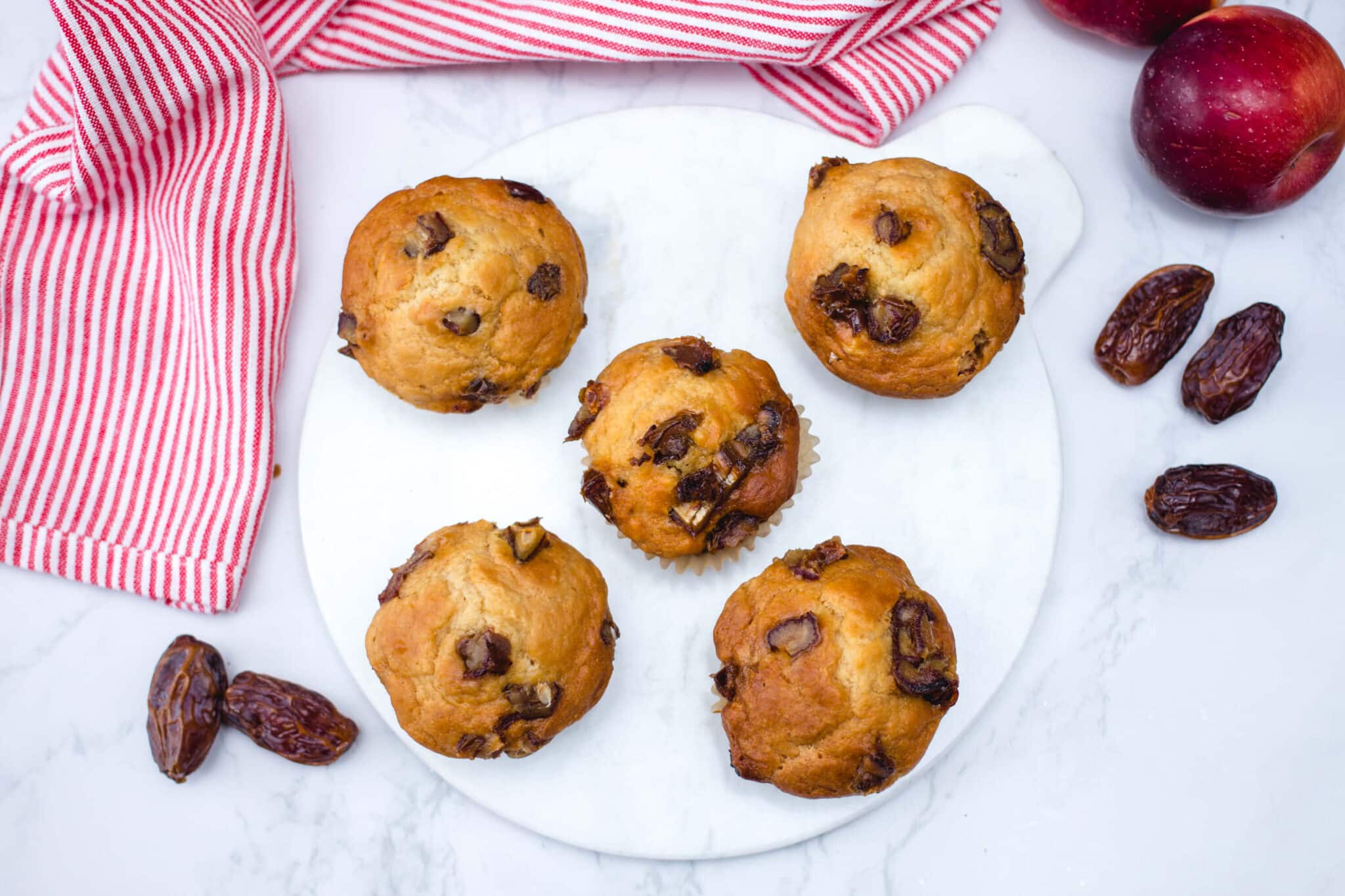 Overhead view of date and apple muffins on a marble board with dates and apples scattered around