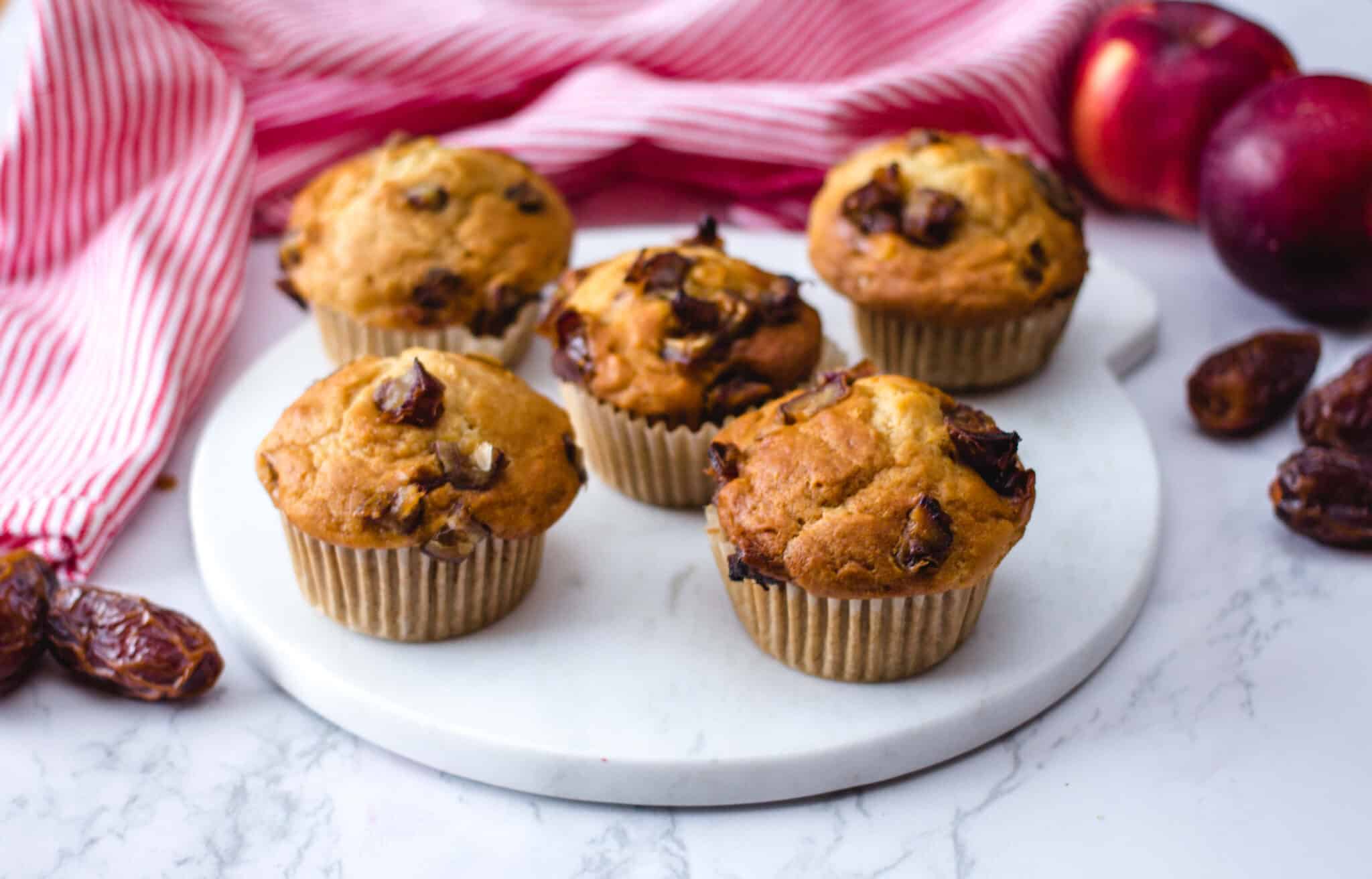 Date and apple muffins on a marble board with whole apples and dried dates in the background