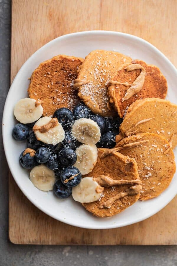 Vegan pumpkin pancakes on a white plate with blueberries, sliced banana and almond butter