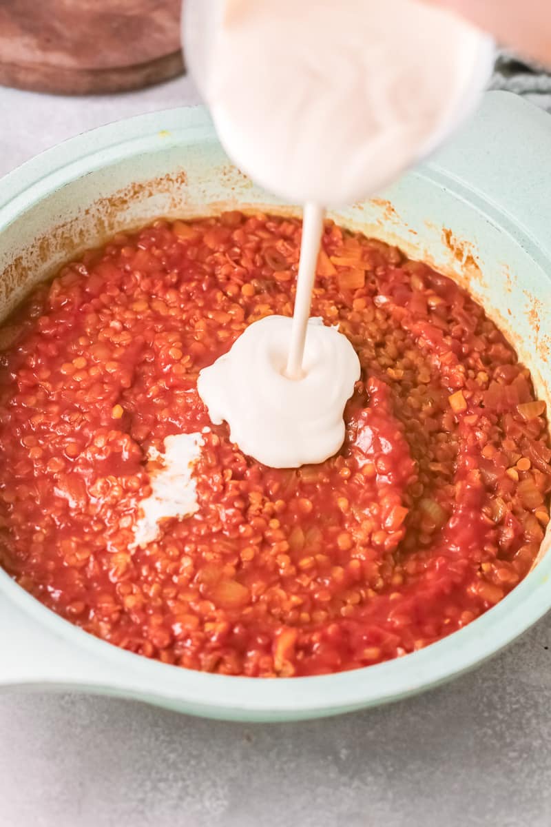 pouring cream into vegan red lentil curry