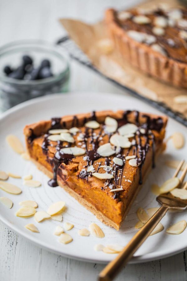 Slice of vegan pumpkin pie drizzled with dark chocolate and topped with sliced almonds