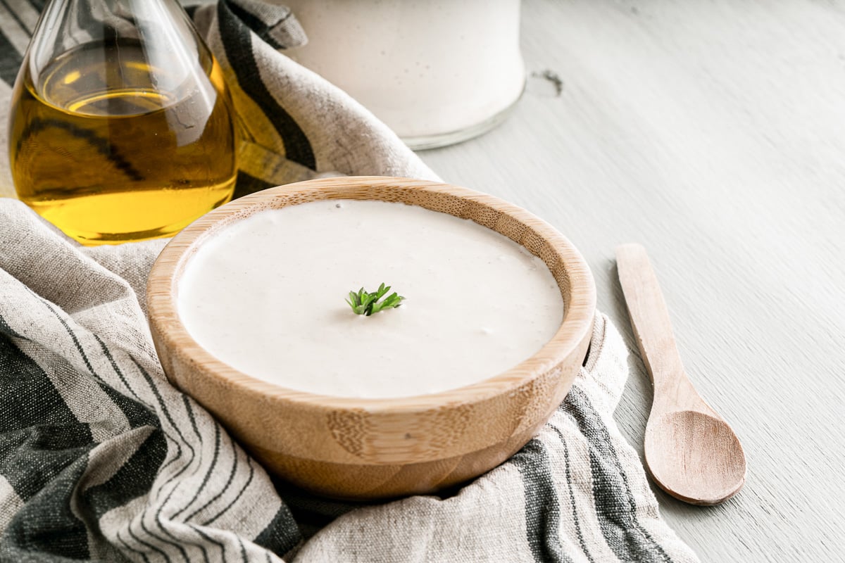 bowl of easy vegan mayo on a dishcloth with a sprig of parsley on top