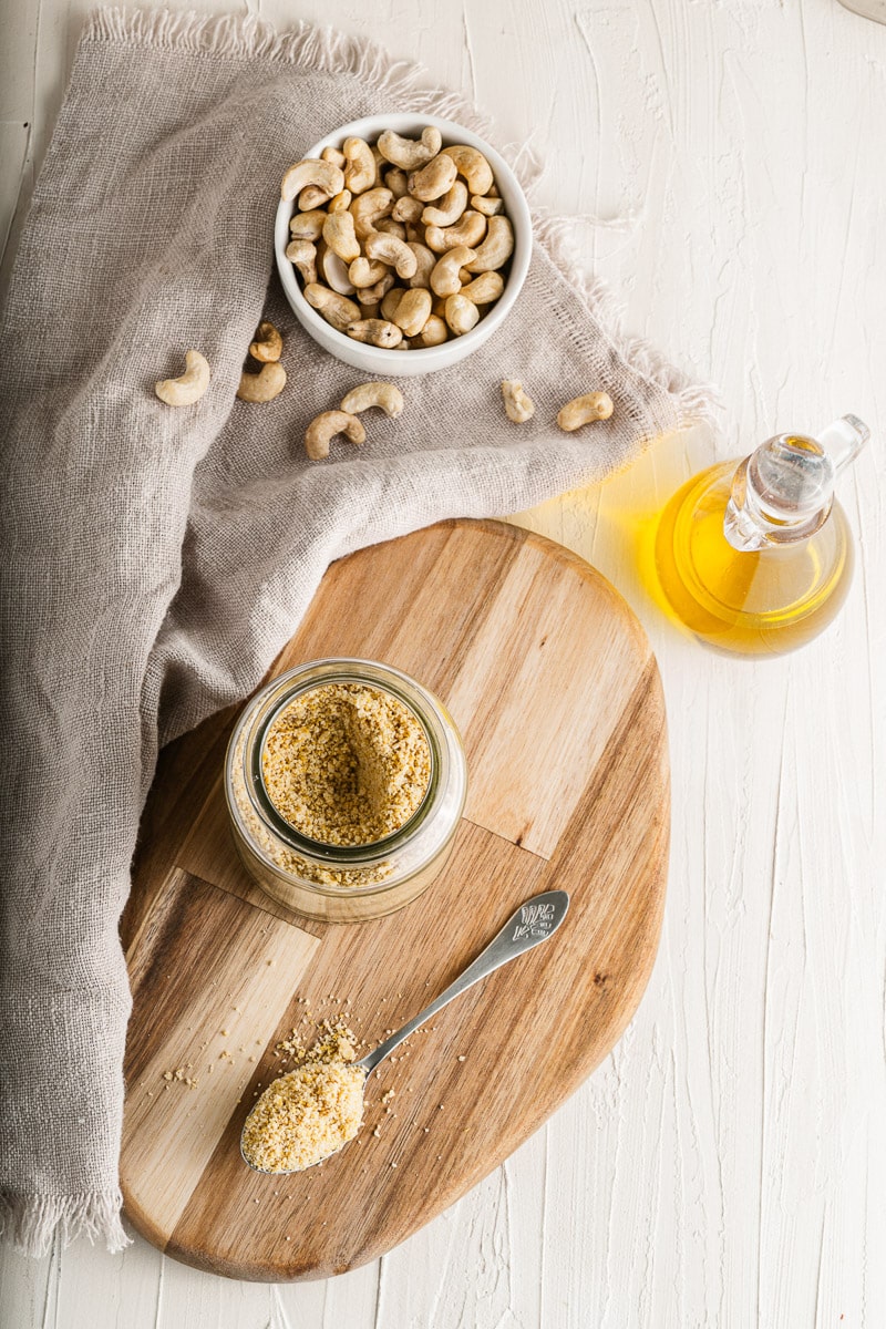 bowl of cashews next to a jar of vegan parmesan