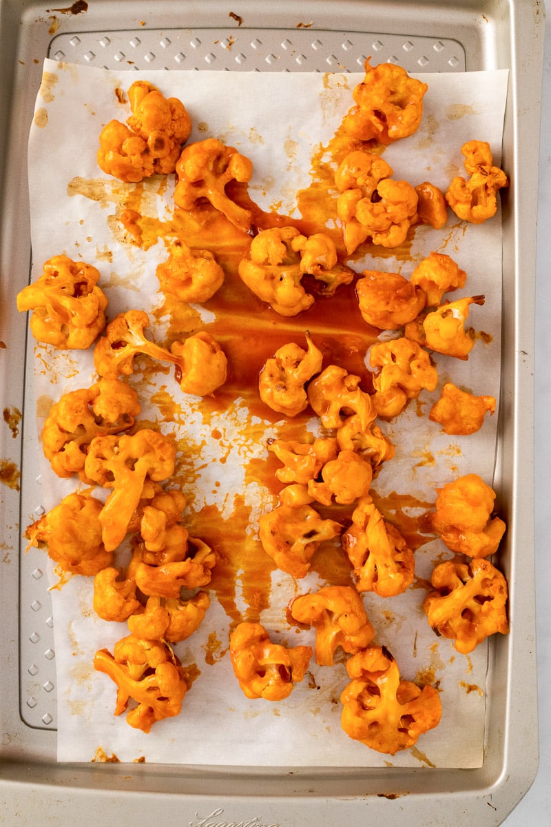 baked buffalo cauliflower bites on baking tray with sauce