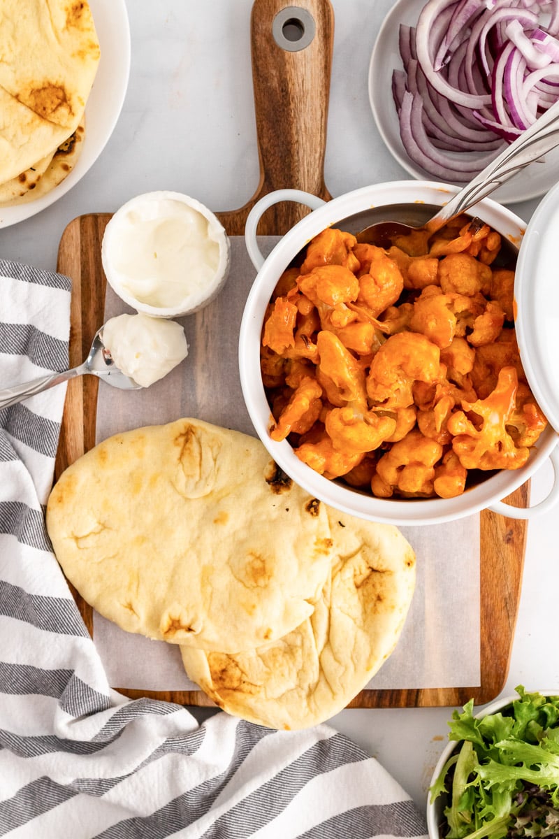 bowl of baked buffalo cauliflower bites next to flatbread on a cutting board