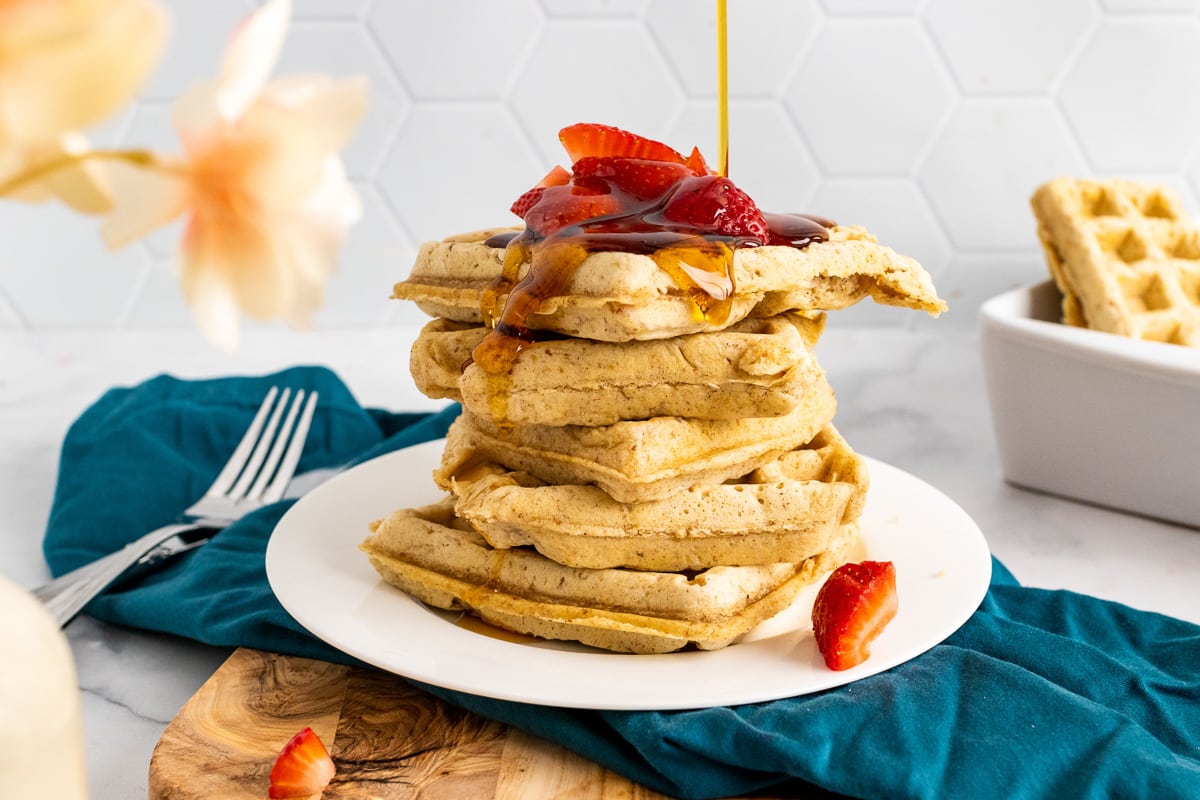 drizzling maple syrup over stack of vegan waffles