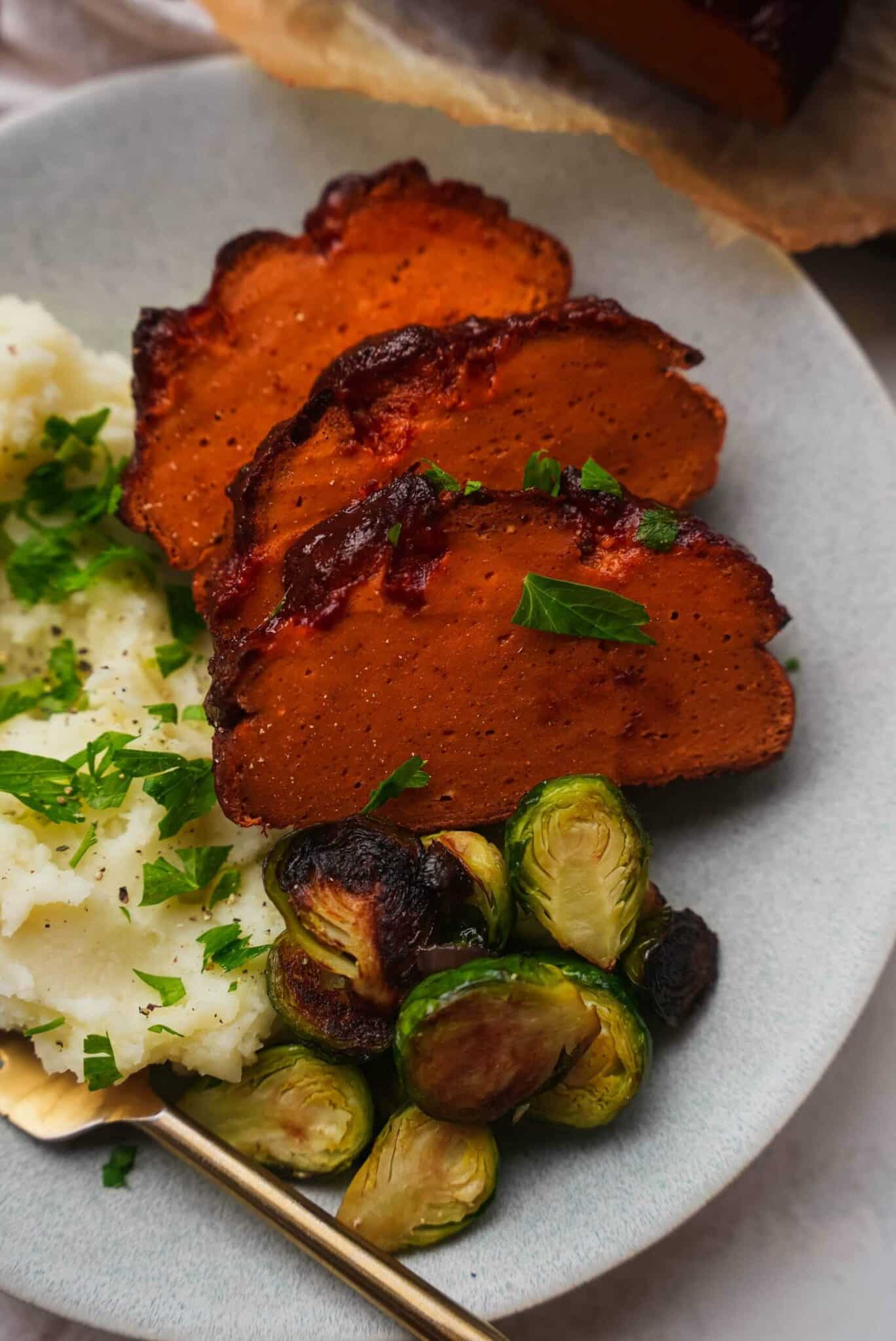 https://ohmyveggies.com/wp-content/uploads/2021/10/Vegan-ham-on-a-plate-with-mashed-potatoes-and-Brussels-sprouts-scaled-1-scaled.jpg