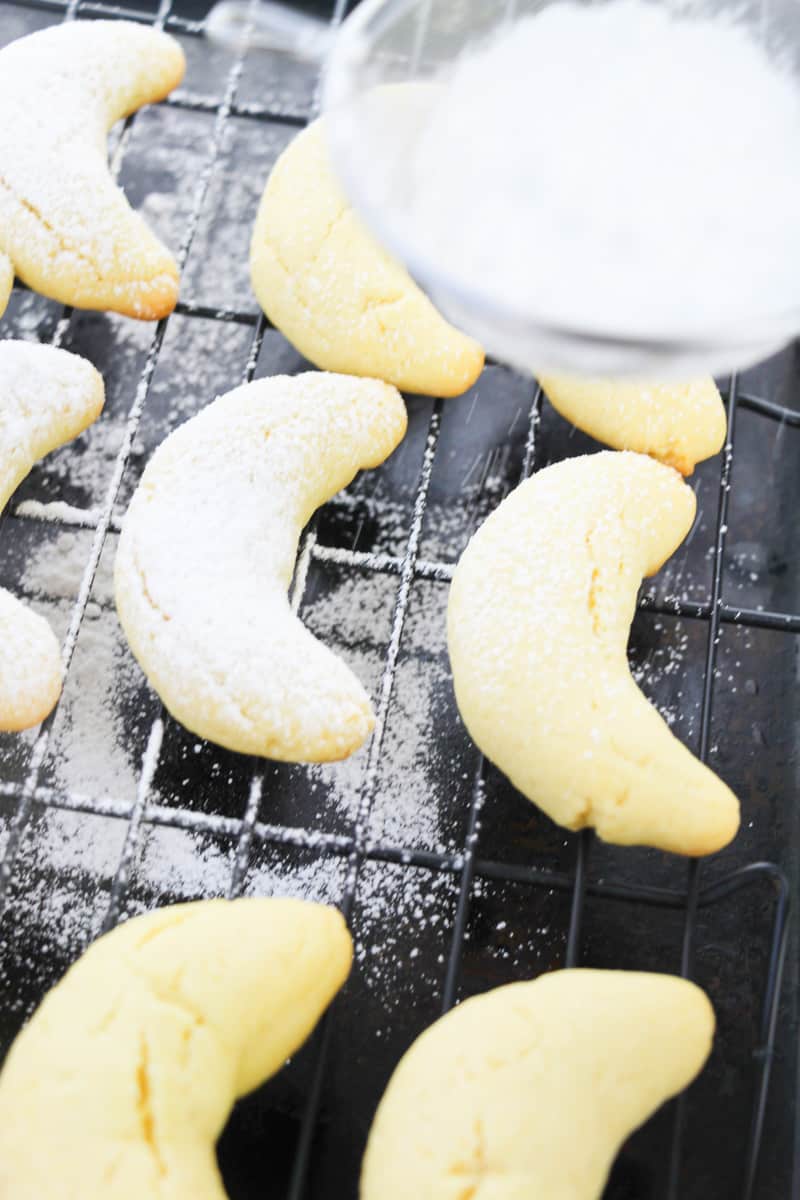 dusting powdered sugar over italian almond crescent cookies