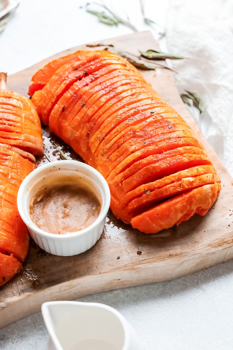 hasselback butternut squash on a wooden board with a small cup of butter