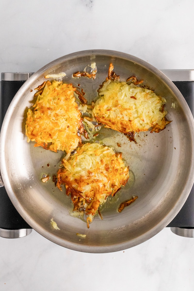 3 potato pancakes frying in metal pan