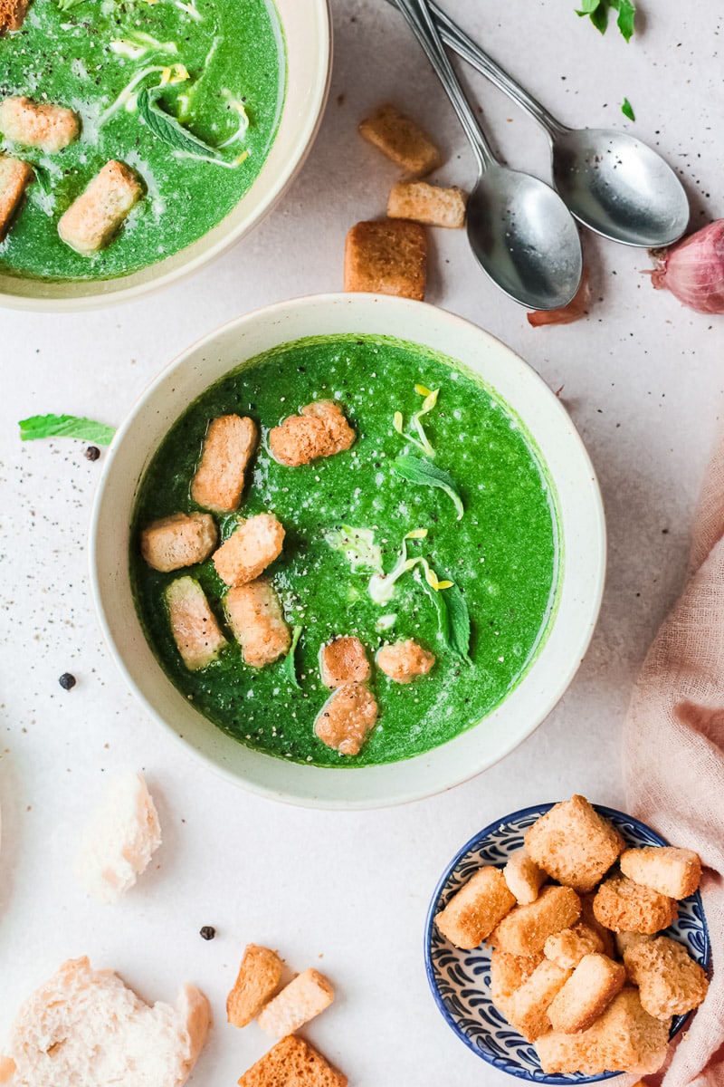 top view two bowls of vegan spinach soup with croutons and two spoons