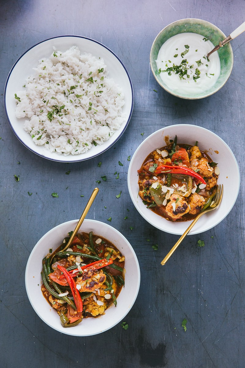 two bowls of veggie curry being served with rice