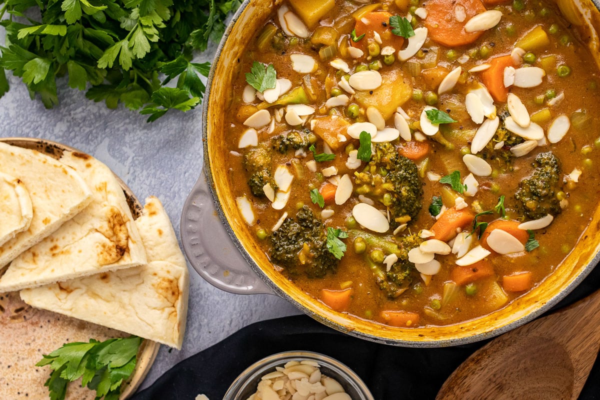 large pot of 30-minute vegetable korma next to plate of naan bread and bunch of cilantro